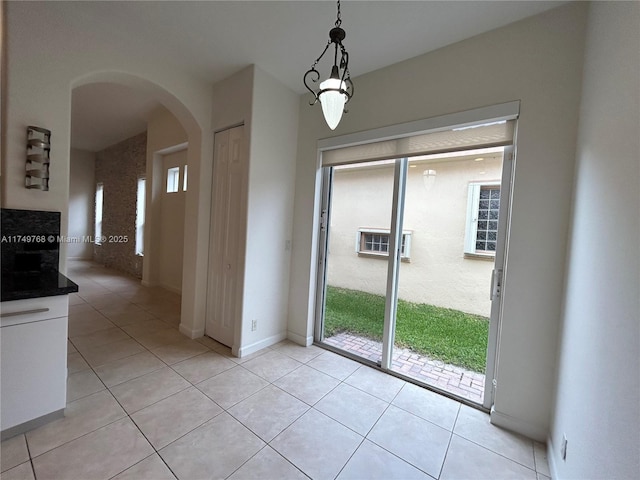 unfurnished dining area with plenty of natural light, arched walkways, baseboards, and light tile patterned flooring