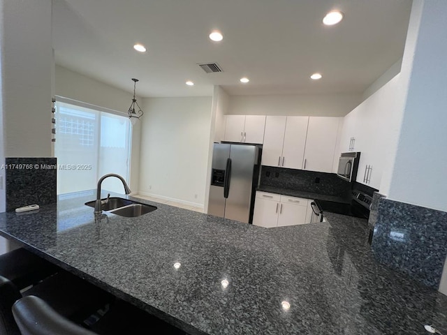 kitchen featuring stainless steel appliances, a peninsula, a sink, visible vents, and dark stone counters