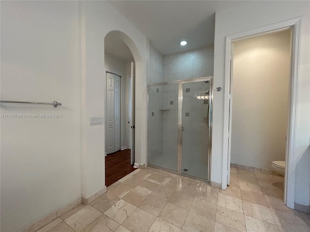 bathroom featuring toilet, a shower stall, and baseboards