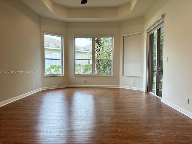 spare room featuring a raised ceiling, dark wood finished floors, and baseboards