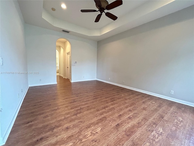 spare room with arched walkways, dark wood finished floors, a raised ceiling, visible vents, and baseboards