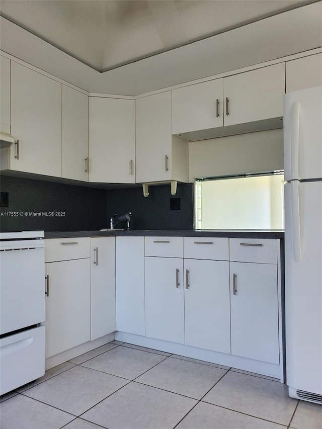 kitchen featuring light tile patterned floors, stove, freestanding refrigerator, tasteful backsplash, and dark countertops