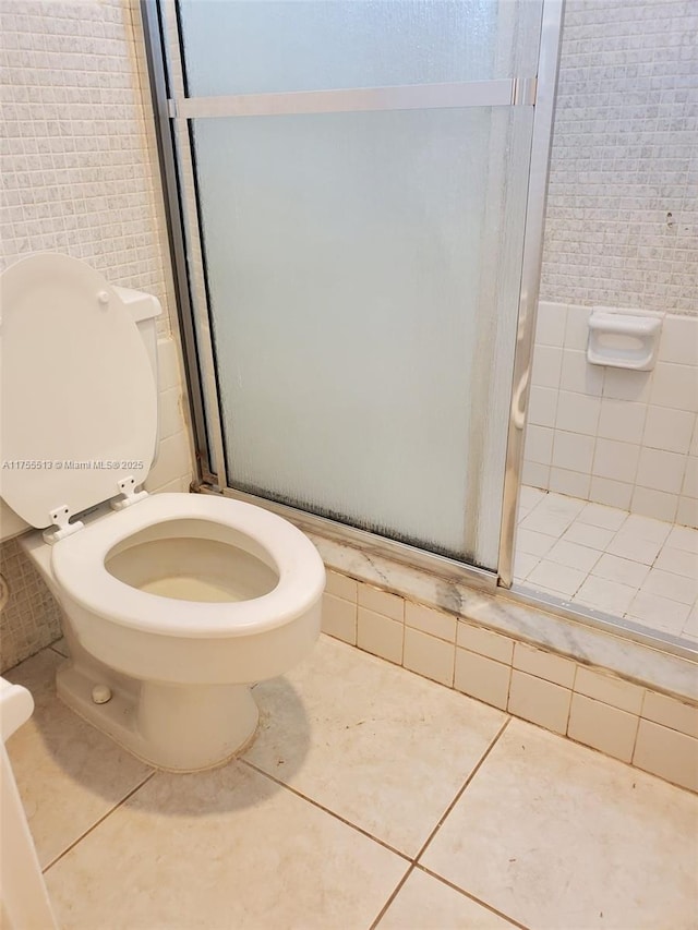 bathroom featuring toilet, a stall shower, tile patterned flooring, and tile walls