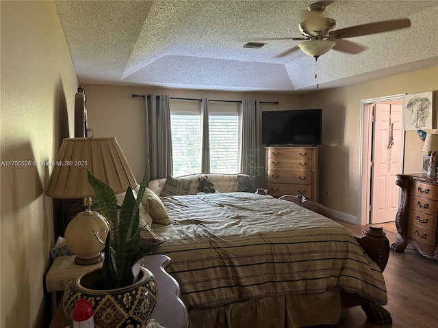 bedroom featuring visible vents, a ceiling fan, a textured ceiling, wood finished floors, and a raised ceiling