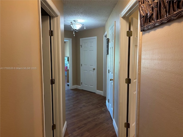 hallway featuring a textured ceiling, dark wood-type flooring, and baseboards