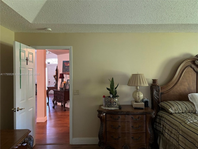 bedroom with a textured ceiling, baseboards, and wood finished floors