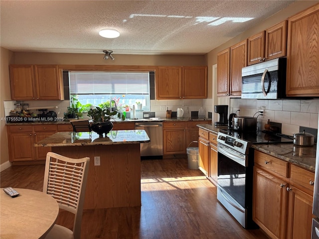 kitchen featuring stone counters, dark wood-type flooring, appliances with stainless steel finishes, and decorative backsplash