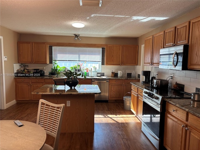 kitchen with a kitchen island, stainless steel appliances, brown cabinetry, decorative backsplash, and dark wood-style flooring