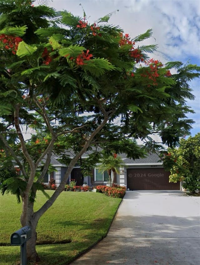 view of property hidden behind natural elements with a front yard, a garage, and driveway