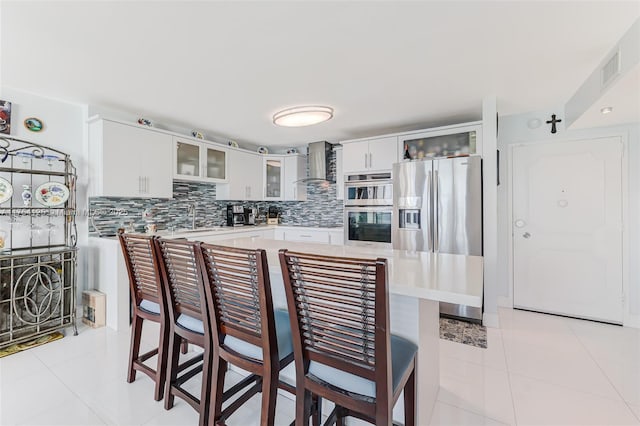 kitchen with stainless steel appliances, light countertops, wall chimney range hood, and light tile patterned floors