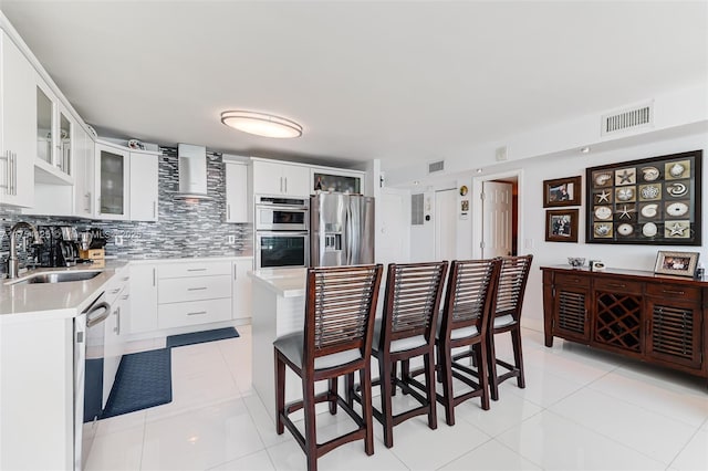 kitchen featuring visible vents, appliances with stainless steel finishes, light countertops, wall chimney range hood, and a sink