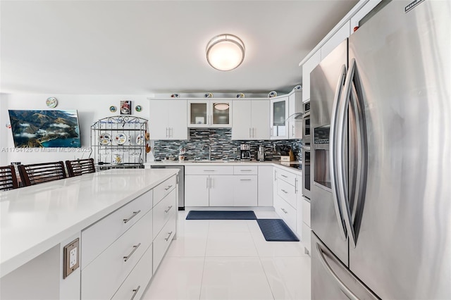 kitchen featuring glass insert cabinets, a sink, stainless steel appliances, light countertops, and backsplash