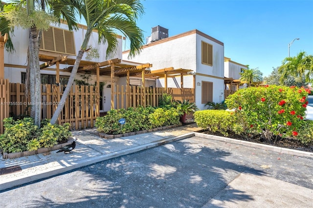 rear view of house featuring stucco siding, a pergola, central AC, fence, and a chimney