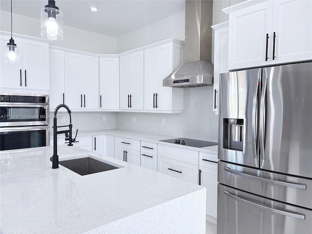 kitchen featuring decorative backsplash, appliances with stainless steel finishes, white cabinets, a sink, and wall chimney exhaust hood