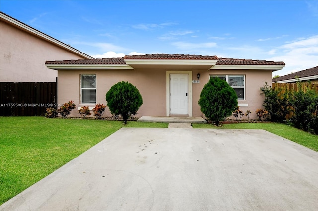 view of front facade with a tiled roof, fence, a front lawn, and stucco siding