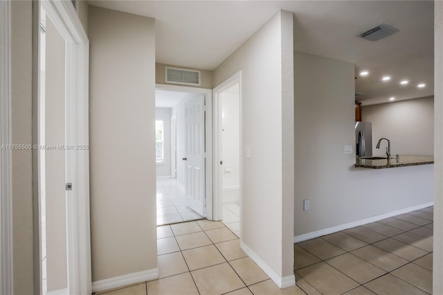 hallway featuring light tile patterned floors, a sink, visible vents, and baseboards