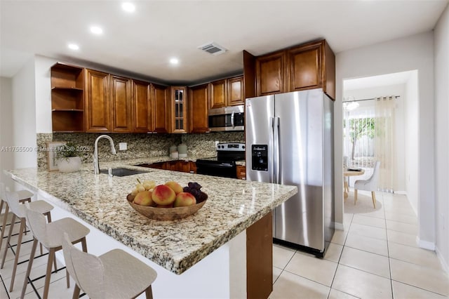 kitchen with appliances with stainless steel finishes, a peninsula, light stone countertops, open shelves, and a sink