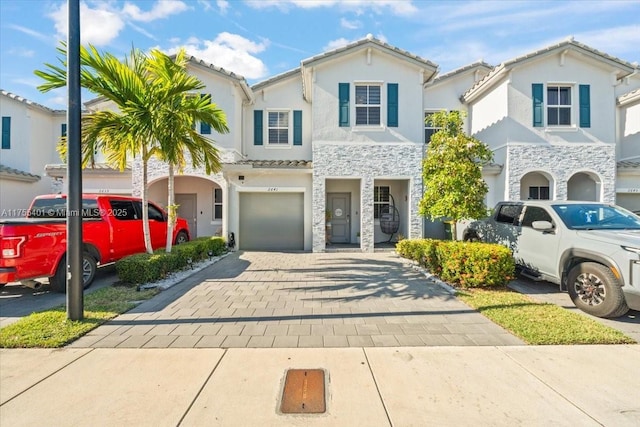 view of front facade with a garage, stone siding, decorative driveway, and stucco siding