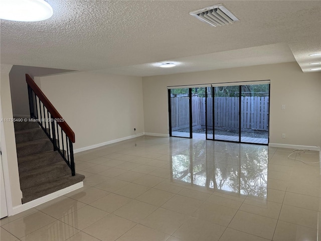 spare room featuring a textured ceiling, light tile patterned flooring, visible vents, baseboards, and stairway