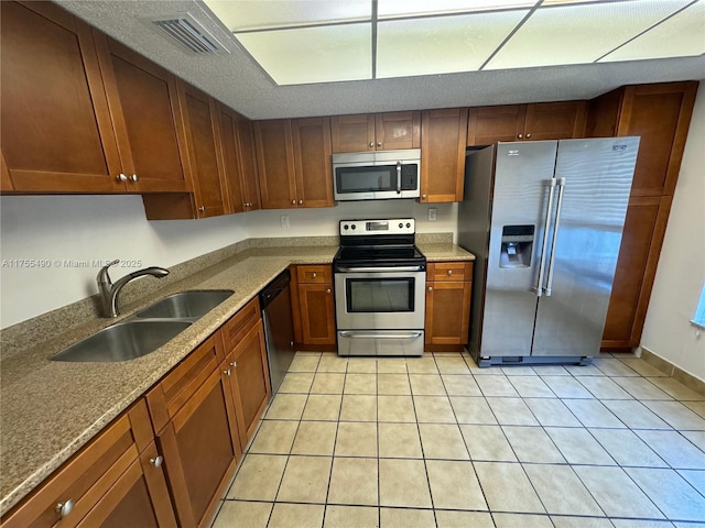 kitchen featuring stone countertops, a sink, visible vents, appliances with stainless steel finishes, and brown cabinetry