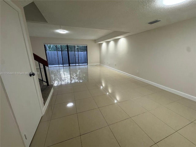 tiled empty room with a textured ceiling, visible vents, and baseboards