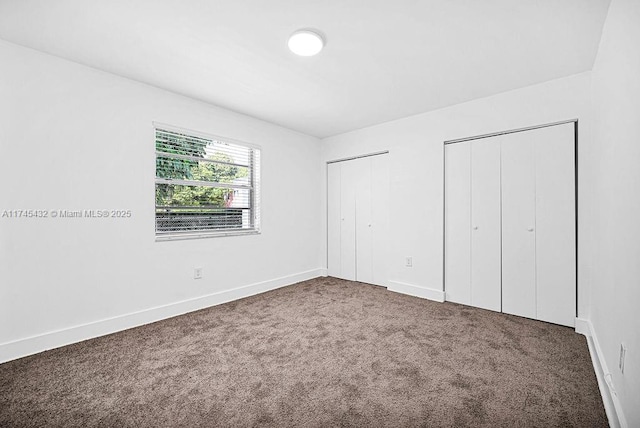 unfurnished bedroom with carpet flooring, baseboards, and two closets