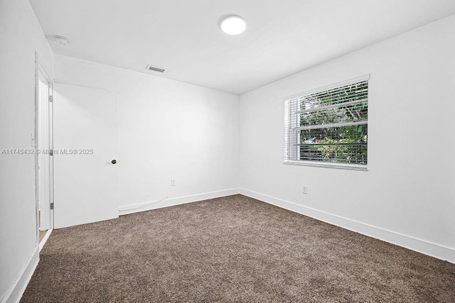 empty room featuring dark carpet, visible vents, and baseboards