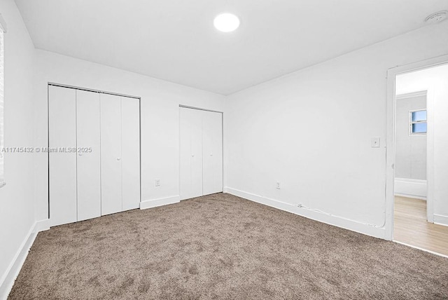 unfurnished bedroom with two closets, baseboards, and carpet flooring