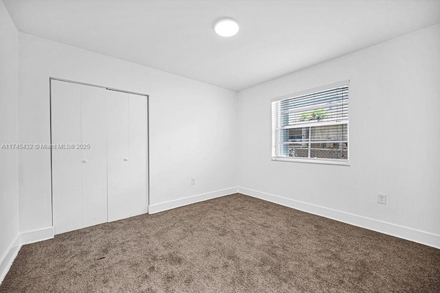 unfurnished bedroom with baseboards, dark carpet, and a closet