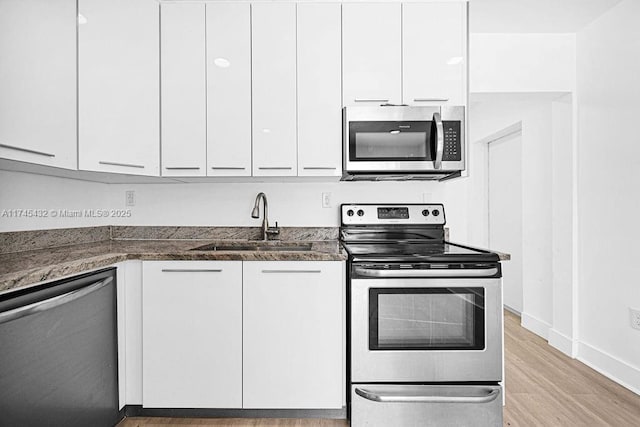 kitchen featuring stainless steel appliances, a sink, white cabinets, light wood-type flooring, and dark stone countertops