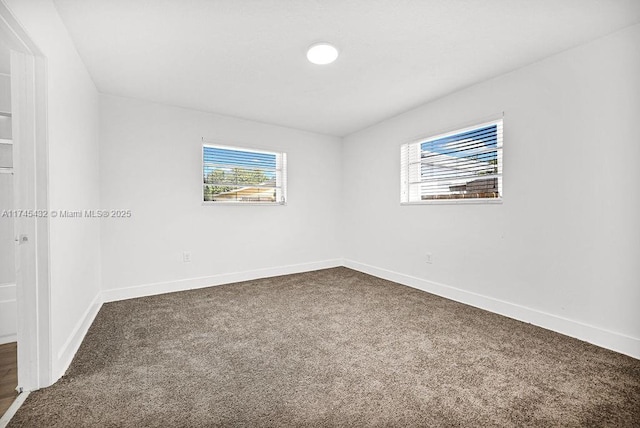 empty room with a healthy amount of sunlight, baseboards, and dark colored carpet