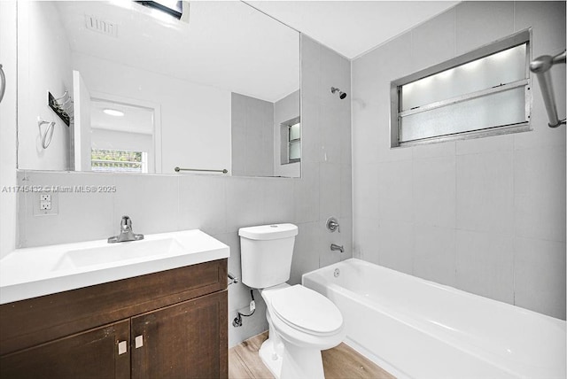 bathroom featuring visible vents, toilet, vanity, shower / washtub combination, and tile walls