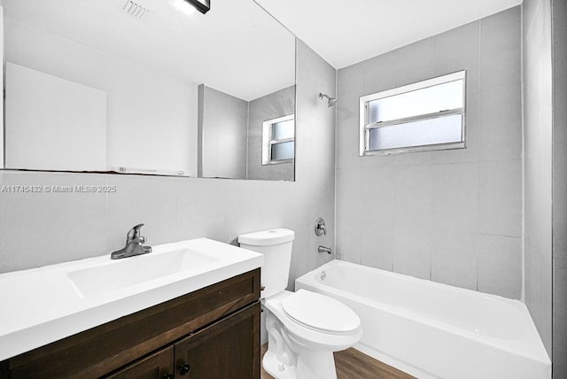 bathroom with tile walls, shower / bathtub combination, visible vents, toilet, and vanity