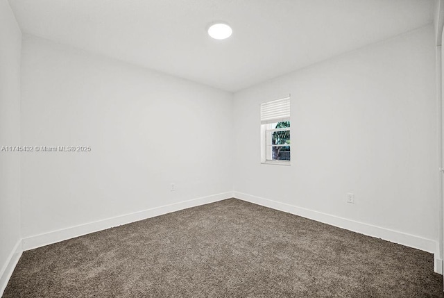 unfurnished room featuring baseboards and dark carpet