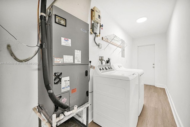 laundry area with laundry area, baseboards, heating unit, light wood-type flooring, and washing machine and dryer