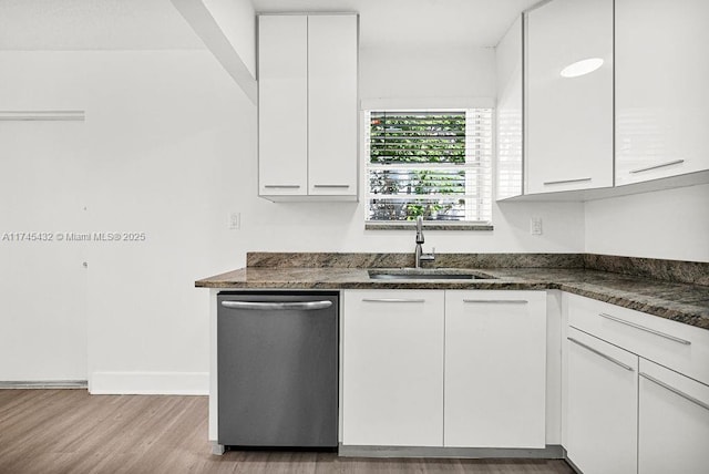 kitchen featuring dark stone countertops, wood finished floors, stainless steel dishwasher, white cabinetry, and a sink