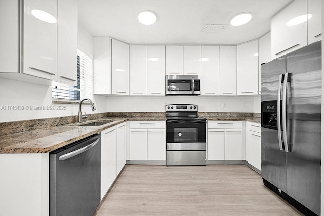 kitchen with dark stone countertops, white cabinetry, appliances with stainless steel finishes, and a sink