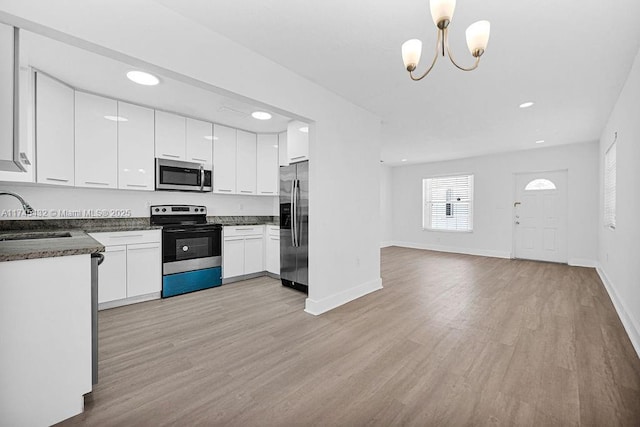 kitchen featuring stainless steel appliances, dark countertops, a sink, and light wood-style flooring