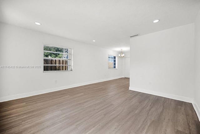 unfurnished room featuring baseboards, recessed lighting, wood finished floors, and an inviting chandelier