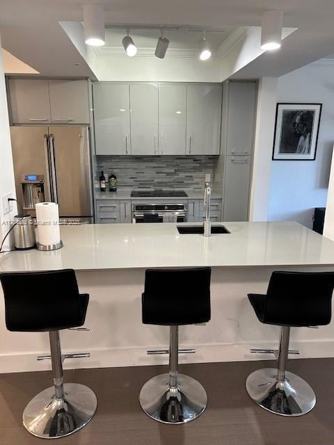 kitchen featuring tasteful backsplash, appliances with stainless steel finishes, a kitchen breakfast bar, gray cabinetry, and a sink