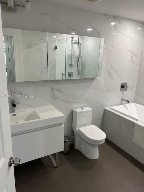 bathroom with toilet, tile walls, a marble finish shower, and vanity