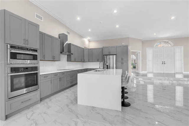 kitchen featuring gray cabinetry, marble finish floor, appliances with stainless steel finishes, light countertops, and wall chimney exhaust hood