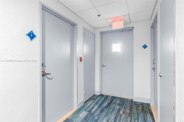 hallway featuring a paneled ceiling, baseboards, and wood finished floors