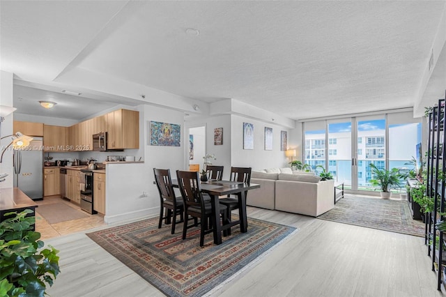 dining room with light wood-style floors, expansive windows, baseboards, and a textured ceiling