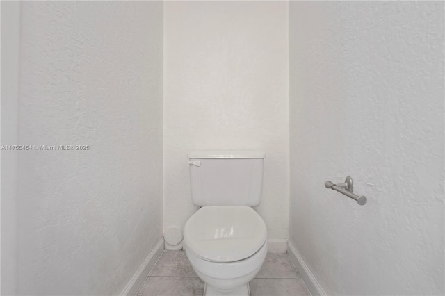 bathroom featuring toilet, a textured wall, baseboards, and tile patterned floors