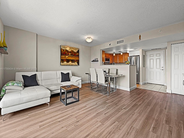 living area featuring light wood-type flooring, baseboards, visible vents, and a textured ceiling