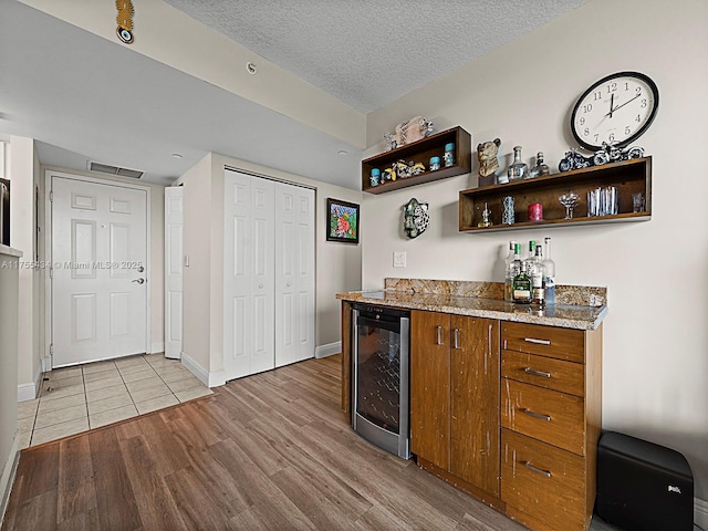 bar featuring a dry bar, beverage cooler, visible vents, a textured ceiling, and light wood-style floors