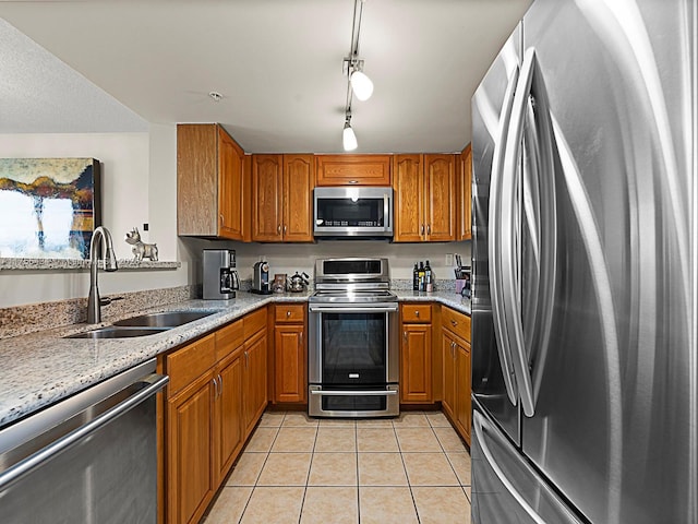 kitchen featuring brown cabinets, light stone countertops, stainless steel appliances, a sink, and light tile patterned flooring