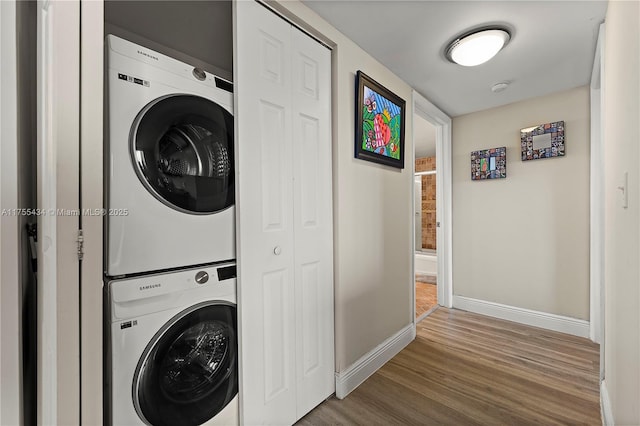 laundry room featuring wood finished floors, stacked washer and clothes dryer, baseboards, and laundry area