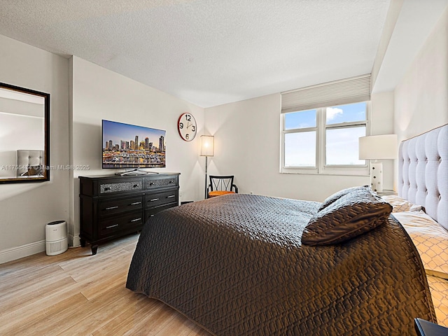 bedroom with a textured ceiling, light wood-style flooring, and baseboards